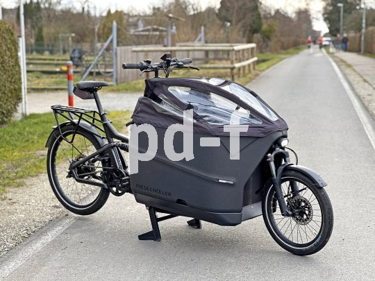 Ein Lastenrad mit verkleidetem Laderaum auf einer Fahrbahn.