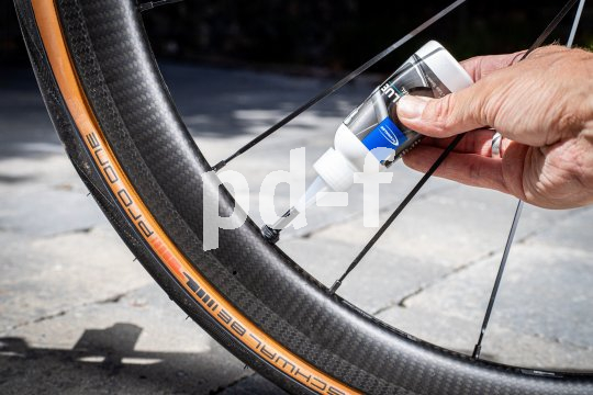 Eine Person füllt eine Flüssigkeit aus einer Kunststoffflasche in das Ventil eines Rennrades.