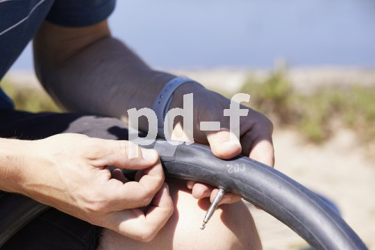 Die Bildunterschrift wird in Bälde eingefügt. Sie können uns aber gern auch per E-Mail oder Telefon kontaktieren, wir helfen gerne weiter. Detailaufnahme einer Person, die einen Flicken auf einen Fahrradschlauch klebt.
