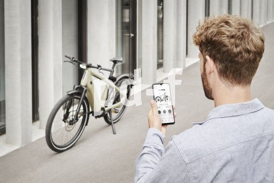 Blick über die Schulter eines Mannes, der auf ein Smartphone schaut. Im Hintergrund steht ein E-Bike vor einem Gebäude.