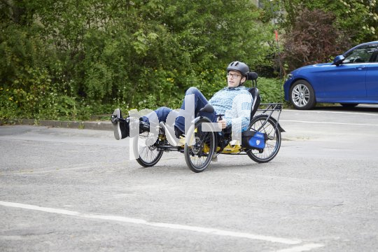 Ein Mann mit Fahrradhelm fährt ein dreirädriges Liegerad auf einem Parplatz.