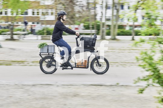 Mit dem Modell CS bietet Ca Go ein wendiges Cargobike, das sich aufgrund seiner kompakten Maße und vielen Zuladungsmöglichkeiten sehr gut für den urbanen Raum eignet. Mann fährt auf voll beladenem Cargobike durch die Stadt.