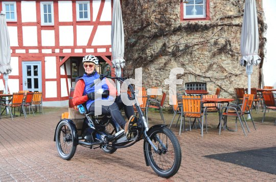 Die Bildunterschrift wird in Bälde eingefügt. Sie können uns aber gern auch per E-Mail oder Telefon kontaktieren, wir helfen gerne weiter. Eine Person auf einem Liegedreirad in einer Altstadt.