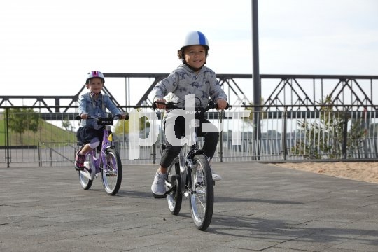 Zwei Kinder fahren auf Fahrrädern über einen Platz.