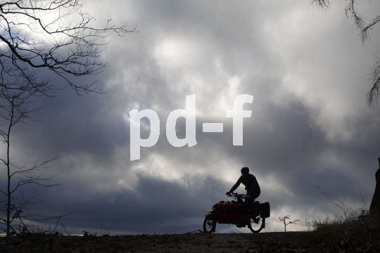 Die Silhouette einer Person auf einem Lastenrad auf dem Horizont vor dunklen Wolken.