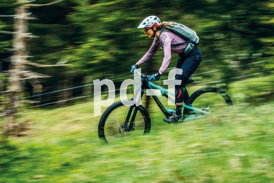 Eine Frau fährt auf einem Mountainbike einen Wiesenweg bergab.