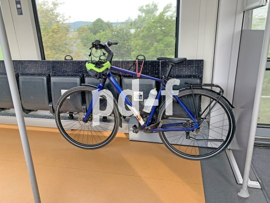 Ein blaues Fahrrad lehnt in einem Zug an Klappsitzen. Am Lenker hängt ein Helm.