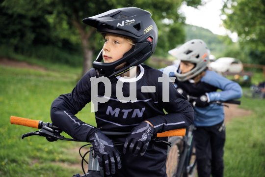 Ein Junge mit Fullface-Helm lehnt auf dem Lenker eines Mountainbikes und schaut sich um.