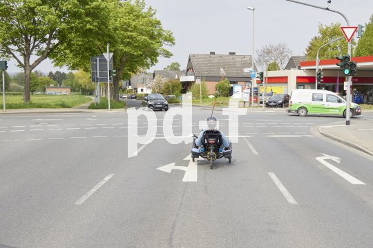 Eine Person auf einem Liegedreirad fährt auf einer Abbiegespur auf eine Straßenkreuzung.