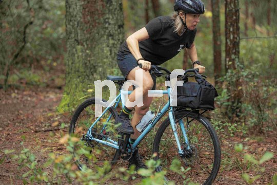 Eine Frau fährt auf einem blauen Fahrrad durch den Wald.
