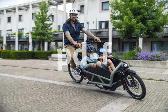 Ein Mann transportiert zwei Kinder in einem Lastenrad.