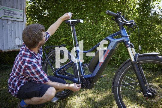 Ein Mann misst an einem E-Bike mit einem Maßband den Abstand zwischen Sattel und Tretlager.