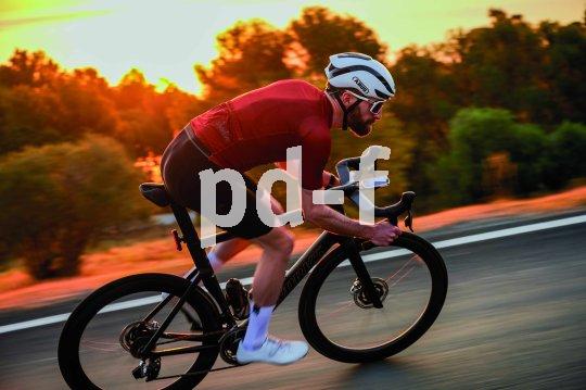 Ein Mann fährt auf einem Rennrad vor der tief stehenden Sonne eine Straße entlang.