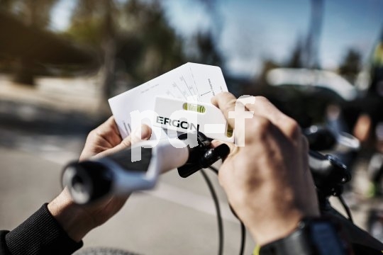Zwei Hände halten eine kleine Wasserwaage und eine Karte mit Grafiken darauf an einen Fahrradlenker.