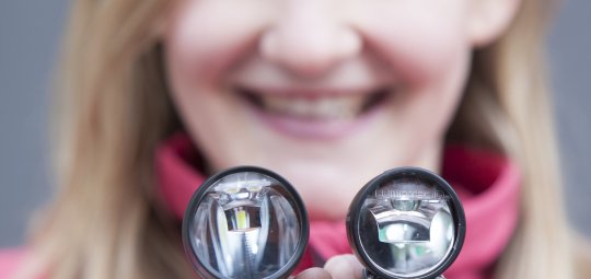 Eine Frau hält zwei Fahrradscheinwerfer vor sich.