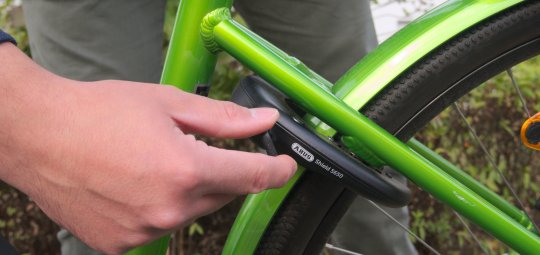 Eine Person hantiert am Schlüssel eines Rahmenschlosses an einem grünen Fahrrad.