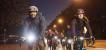 Eine Gruppe Radfahrer:innen mit deutlich sichtbarer Beleuchtung fährt bei Dunkelheit auf einer Straße auf die Kamera zu.