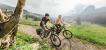 Zwei Personen auf E-Bikes in einer Gebirgslandschaft.