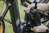 Eine Person hält einen Akku neben ein E-Bike.