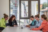 Fünf Frauen sitzen an einem Tisch und schauen Dokumente an. Hinter ihnen sind durch Fenster Kletterwände zu sehen.