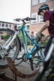 Ein Kind nimmt das Schloss von der Sattelstütze eines blauen Fahrrades in einem Fahrradständer.