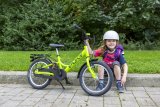 Ein Kind sitzt neben einem grünen Kinderrad auf einer Bordsteinkante.