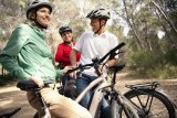 Drei lachende Personen mit E-Bikes im Wald.