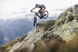 Mann springt mit E-Mountainbike über ein Hindernis in den Bergen.