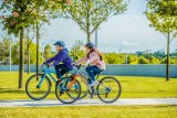 Zwei Kinder fahren auf Fahrrädern einen Betonweg zwischen Rasenflächen entlang.