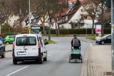 Ein weißes Auto überholt eine Person auf einem Fahrrad mit Anhänger auf einer Straße ohne Fahrradspur in einem Wohngebiet.