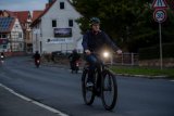 Ein Mann fährt in der Dämmerung mit dem Fahrrad auf einer Straße. Sehr deutlich zu sehen ist der leuchtende Frontscheinwerfer.