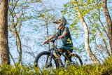 Ein Kind mit Fullface-Helm und einem Mountainbike zwischen Bäumen.