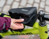 Eine Person öffnet oder schließt eine kleine Fahrradtasche auf dem Oberrohr eines Fahrrades.