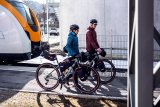 Zwei Personen schieben Fahrräder mit Gepäck daran von einem Zug weg.
