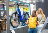 Mehrere Personen betrachten ein blaues E-Bike an einem Messestand.