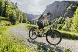 Eine Frau fährt auf einem E-Bike einen Schotterweg im Gebirge entlang.