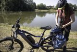 Eine Frau steht neben einem E-Bike und packt etwas in oder aus einer von zwei Packtaschen am Gepäckträger.
