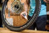 Eine Person hält das Hinterrad eines Mountainbikes auf einer Werkbank und setzt eine kleine Plastikflasche mit Dichtflüssigkeit an das Ventil an.