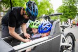 Ein Mann schnallt zwei Kinder in einem Lastenrad an.