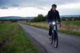 Ein Mann fährt in der Dämmerung eine schmale Landstraße mit einem beleuchteten Fahrrad entlang.