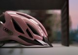 Ein rosa Fahrradhelm mit dem Logo der Firma Abus darauf, von der Seite betrachtet.