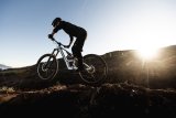 Eine Person fährt in offener Gebirgslandschaft vor der tiefstehenden Sonne ein E-Mountainbike.