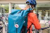 Blick auf einen Rucksack, getragen von einer Radfahrerin, die scheinbar gerade ihr Fahrrad abstellt.