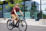 Ein Mann fährt auf einem E-Bike vor einem Gebäude mit Glasfassade entlang.