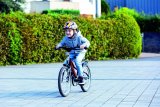 Ein Kind mit buntem Helm fährt mit einem Fahrrad über einen Platz.