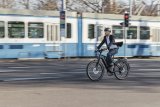 Ein Mann fährt auf einem E-Bike durch die Stadt. Im Hintergrund: eine weiß-blaue Straßenbahn.