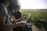 Eine Frau und ein Mann stehen vor einem Feld und betrachten eine Karte. Beide tragen Fahrradhelme.
