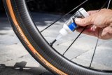 Eine Person füllt eine Flüssigkeit aus einer Kunststoffflasche in das Ventil eines Rennrades.