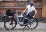 Eine Person steht neben einem E-Bike und befestigt eine Tasche auf dem Gepäckträger.