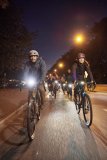 Eine Gruppe Radfahrer:innen mit deutlich sichtbarer Beleuchtung fährt bei Dunkelheit auf einer Straße auf die Kamera zu.